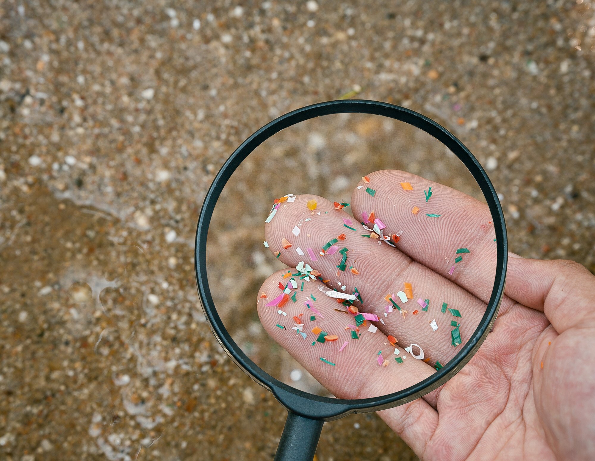 View through magnifying glass of fingers covered in microplastic particles